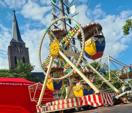 Riesenrad - Miniriesenrad Riesenrad mit bunten Gondeln vor einer Kirche bei blauem Himmel.