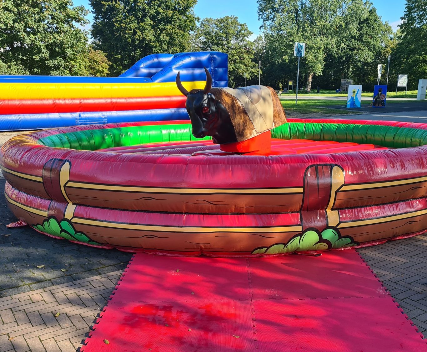 Bullriding - Rodeo Ein Mechanischer Bulle in einem bunten, gepolsterten Rundbecken auf einem Festgelände.