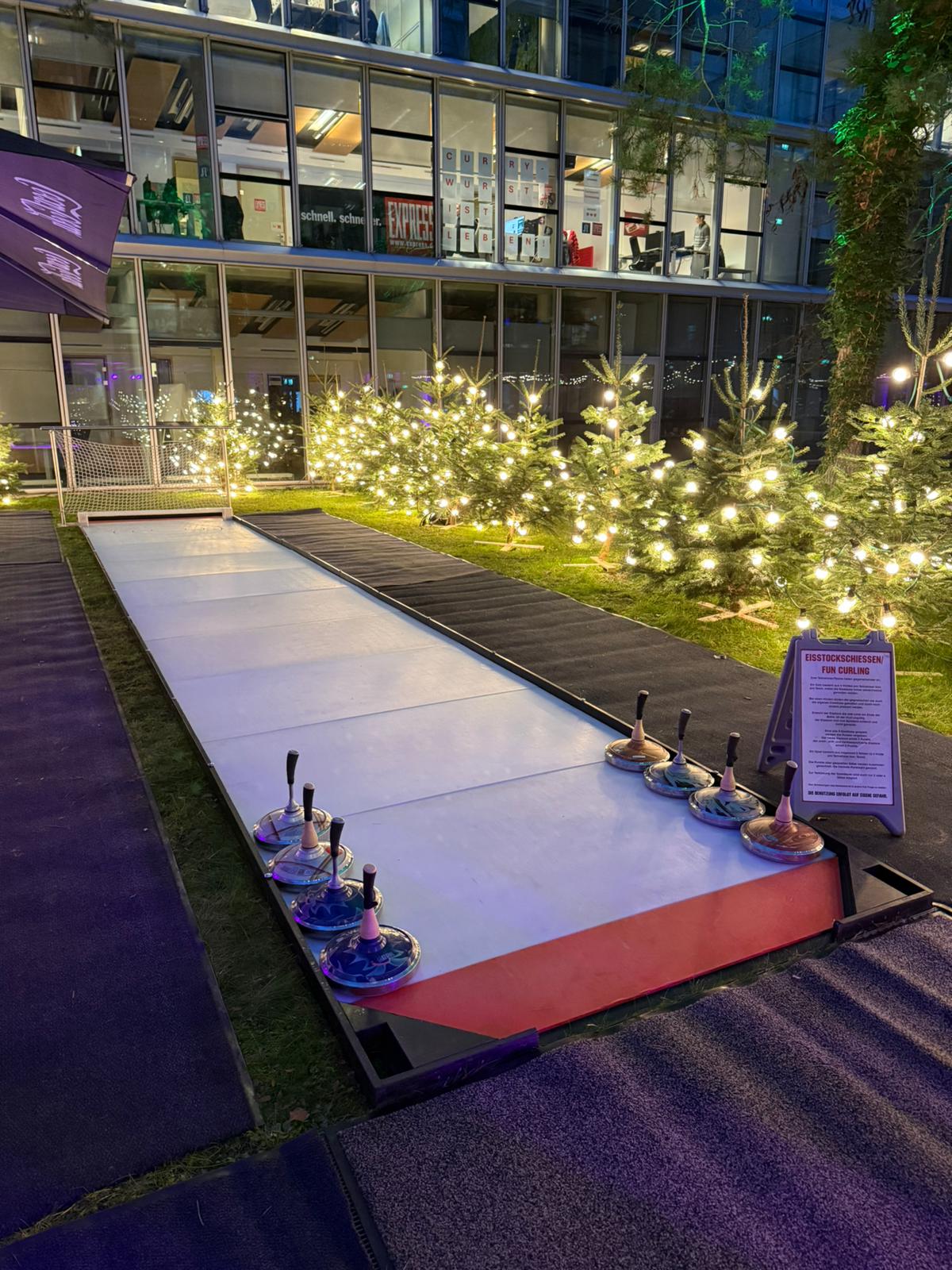 Eisstockschiessen - Fun Curling Rutschbahn mit Weihnachtsbeleuchtung und Lichtern in einem urbanen Garten.