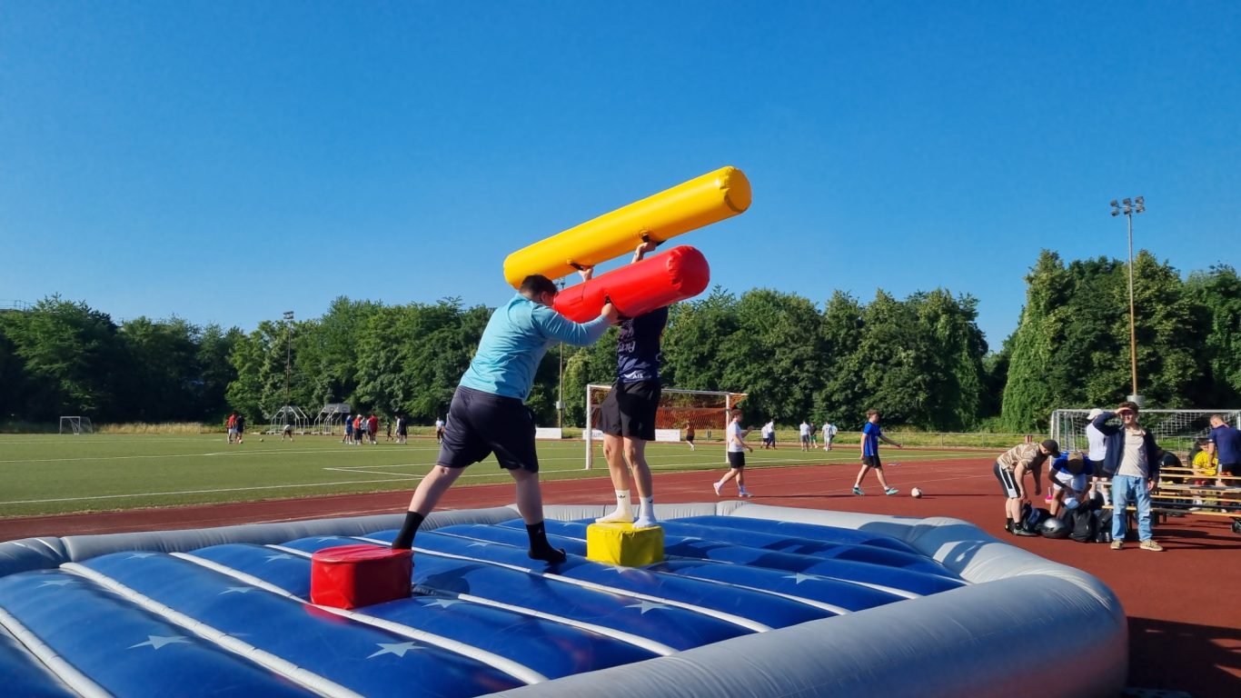 Gladiator Fight - Gladiatoren Arena Zwei Personen kämpfen auf einer aufblasbaren Arena mit großen, bunten Schaumstoffstöcken.