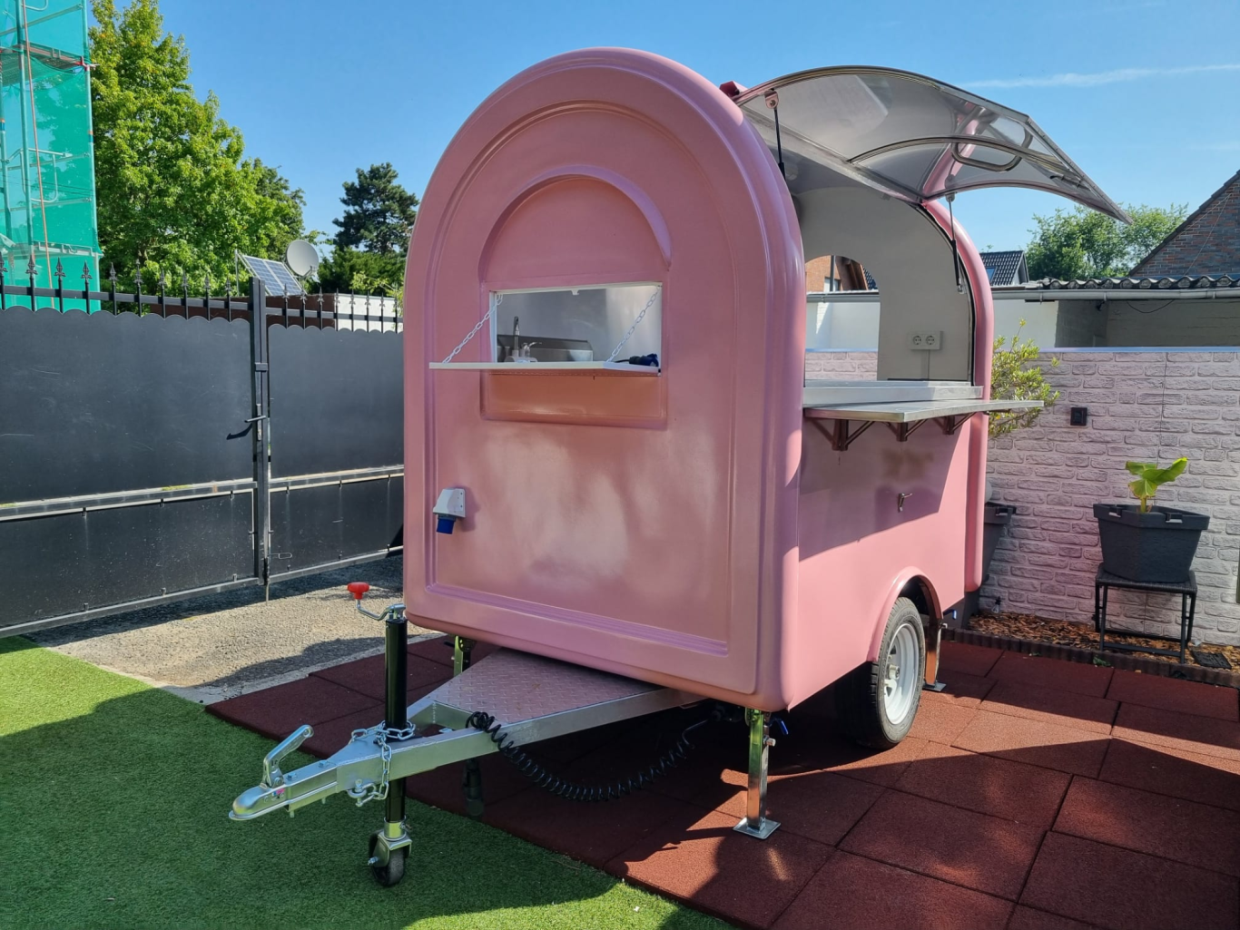 Retro-Foodtrailer Rosa Verkaufsanhänger mit geöffnetem Dach und Verkaufsfenster, auf grünem Rasen.