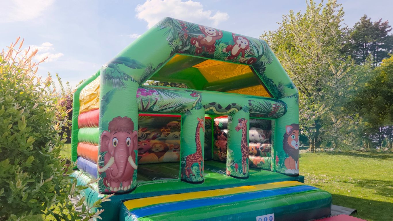 Hüpfburg Jungle mit Überdachung Bunte Hüpfburg mit Tiermotiven in einem Garten unter blauen Himmel.