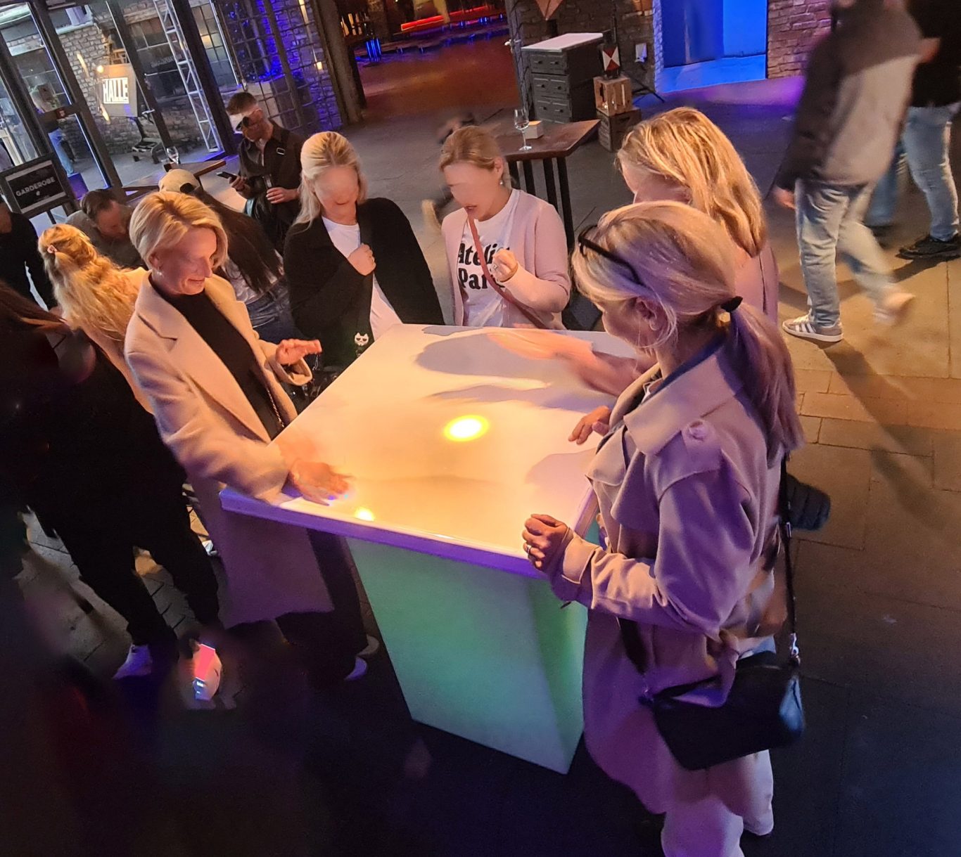 Reaktionstisch - Reaction Desk Fünf Personen stehen um einen beleuchteten Tisch in einer belebten Umgebung.