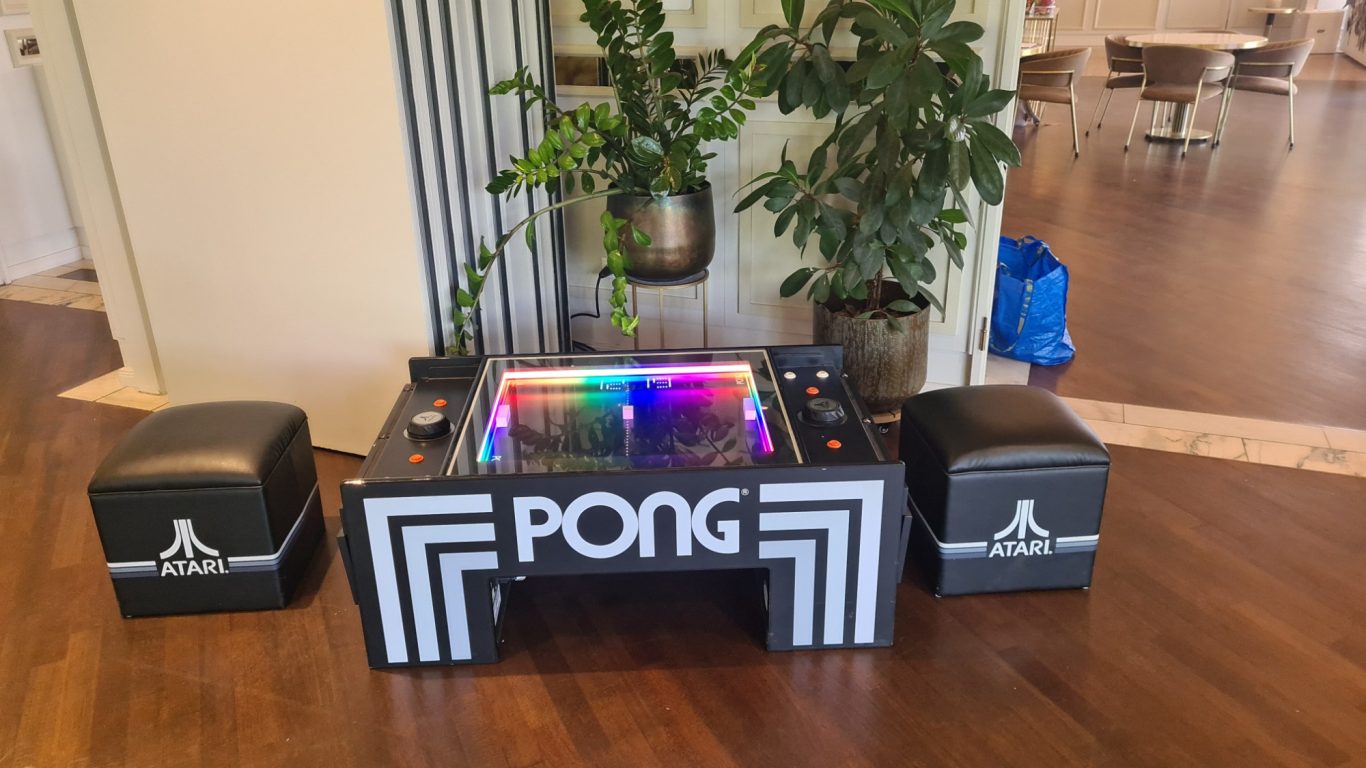 Tisch Pong - ATARI PONG Pong-Spieltisch mit bunter Beleuchtung und zwei Sitzwürfeln daneben.